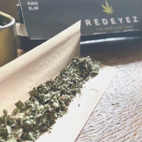 CBD hemp buds ready to be rolled with a paper rizla, next to Redeyez packet with logo and cannabis tin helping to reduce stoner stigma
